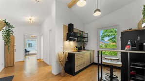 Una cocina moderna con suelo de madera, encimera negra y taburetes de bar. Se ve una ventana con vistas a zonas verdes.