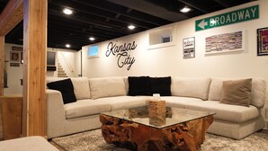 A modern living room with a sectional sofa, a glass coffee table, and a wall sign reading "Kansas City." - Modern Mission Escape Home - Family Friendly - Close to All Attractions (Mission)