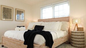 A bed with a wooden frame, white bedding, and a black throw blanket. There are two framed pictures on the wall, a bedside lamp, and a window with blinds. - Modern Mission Escape Home - Family Friendly - Close to All Attractions (Mission)