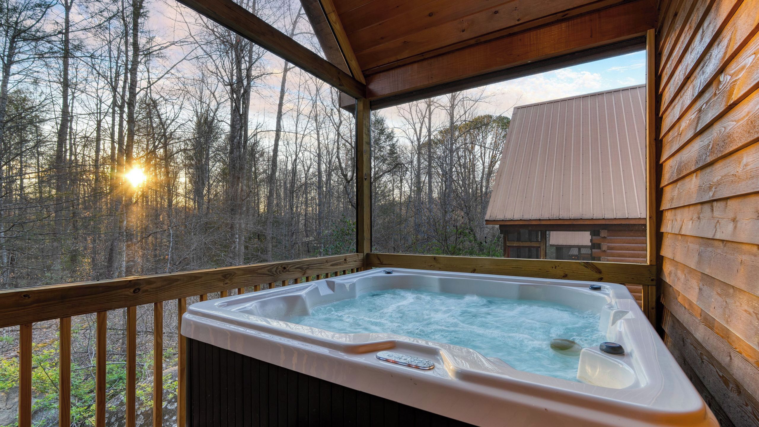 A wooden deck with a hot tub, surrounded by trees and a cabin.