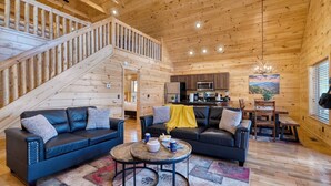 A wooden cabin interior with a staircase, two sofas, a dining table, and a kitchen area. - Hot Tub + Foosball Access to Pool, Tennis, Gym Chill'n in the Smokies (Gatlinburg)