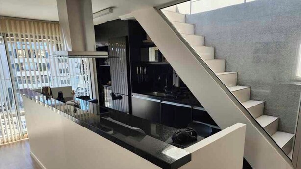 A modern kitchen with a central island, a staircase, and a view of the city.