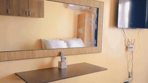 Una habitación de hotel moderna con un espejo grande, un televisor de pantalla plana montado en la pared, una mesita de noche y un banco acolchado.