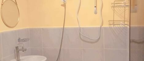 Ett badrum med ett vitt handfat, ett duschmunstycke som kan hållas i handen och en väggmonterad kontrollpanel.