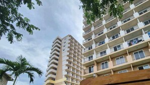 Un edificio residencial de varios pisos con balcones, un área verde y un banco.