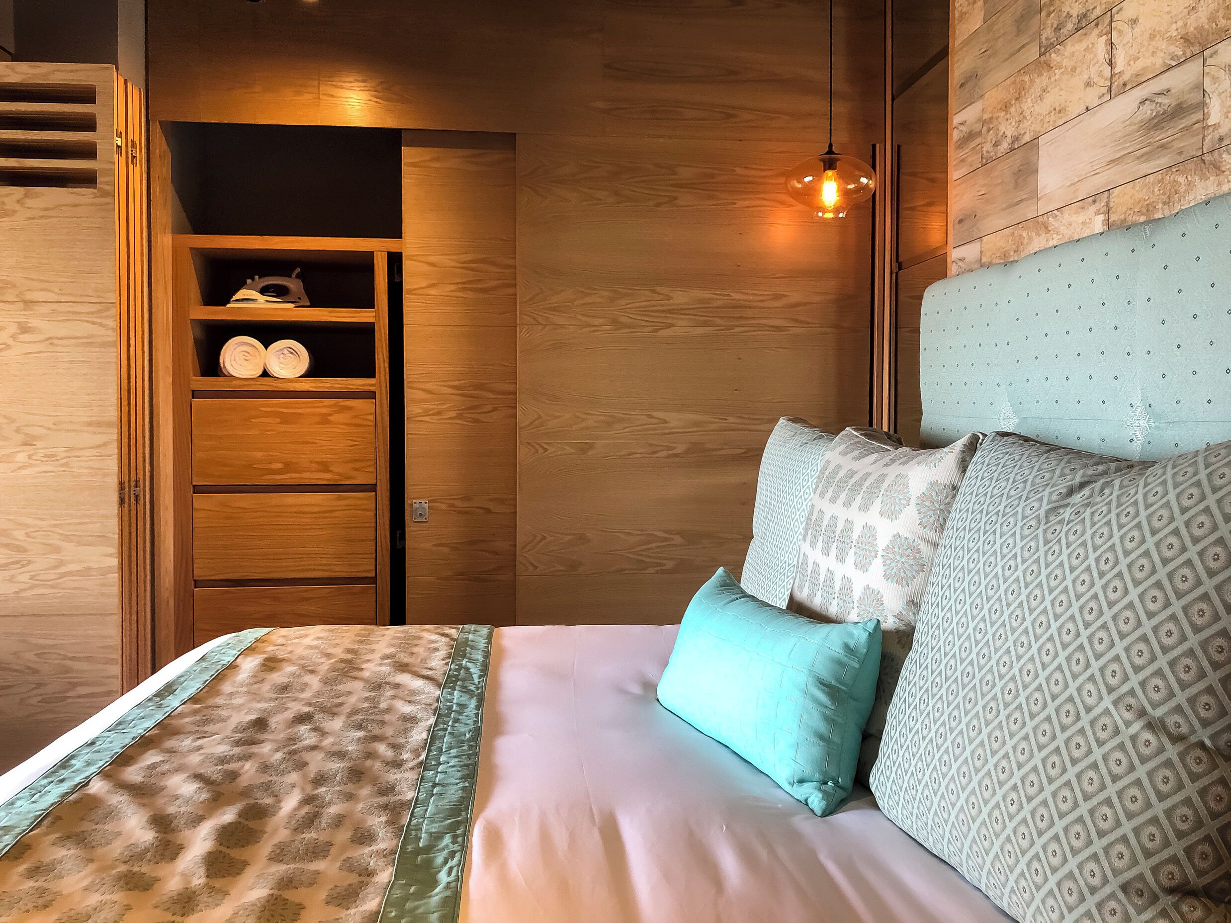 Un dormitorio con un armario de madera, una cama con ropa de cama estampada y una lámpara colgante.
