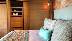 Ein Schlafzimmer mit einem hölzernen Kleiderschrank, einem Bett mit gemusterten Textilien und einer hängenden Deckenleuchte.
