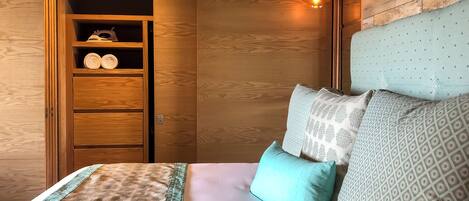 Un dormitorio con un armario de madera, una cama con ropa de cama estampada y una lámpara colgante.