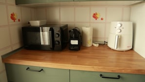Una cocina con microondas, cafetera y un electrodoméstico blanco, posiblemente una cocedora de arroz, sobre una encimera de madera.