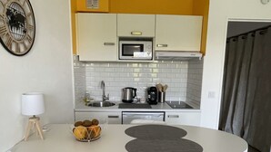 Een kleine keuken met een magnetron, waterkoker en koffiezetapparaat. Er is een zithoekje met een tafel en twee stoelen.