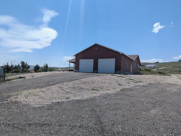 A single-story red building with two white garage doors, a gravel driveway, and a clear blue sky.