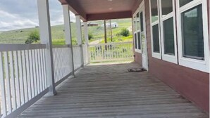 A covered porch with a wooden deck, white railings, and large windows. - Charming 3-bedroom house with AC, WiFi in beautiful Lander (Lander)