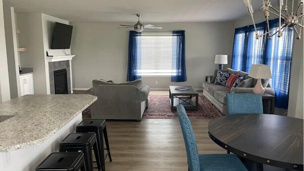 A modern living room with a sofa, a dining table with chairs, a kitchen area with a countertop and stools, and a ceiling fan. - Charming 3-bedroom house with AC, WiFi in beautiful Lander (Lander)