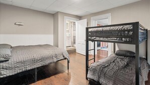 Una habitación con dos camas, una de ellas litera, techo blanco y una puerta que da a un baño.