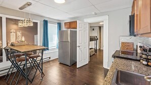 Una cocina moderna con un refrigerador de acero inoxidable, una mesa de comedor de madera con sillas y una lámpara colgante.