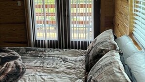 A wooden cabin room with a bed, a window with blinds, and a view of a wooden deck outside. - Cozy 2 bedroom cottage with heated pool AC in charming New Hope (New Hope)