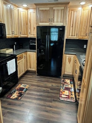 Una cocina con armarios de madera, un refrigerador negro, una estufa y un microondas.