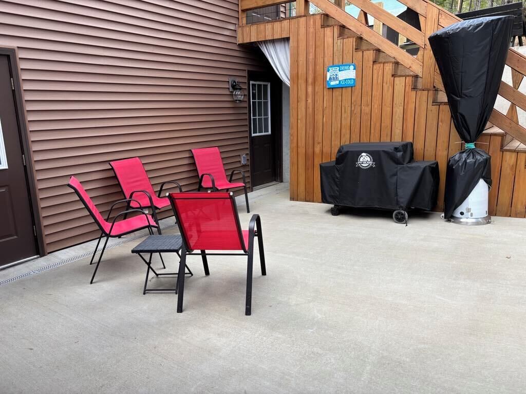 A patio area with red and black chairs, a barbecue grill, and a covered table.