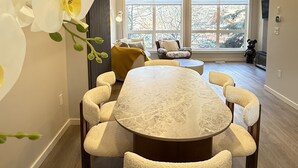 A modern dining area with a round table and chairs, large windows, and a view of trees.