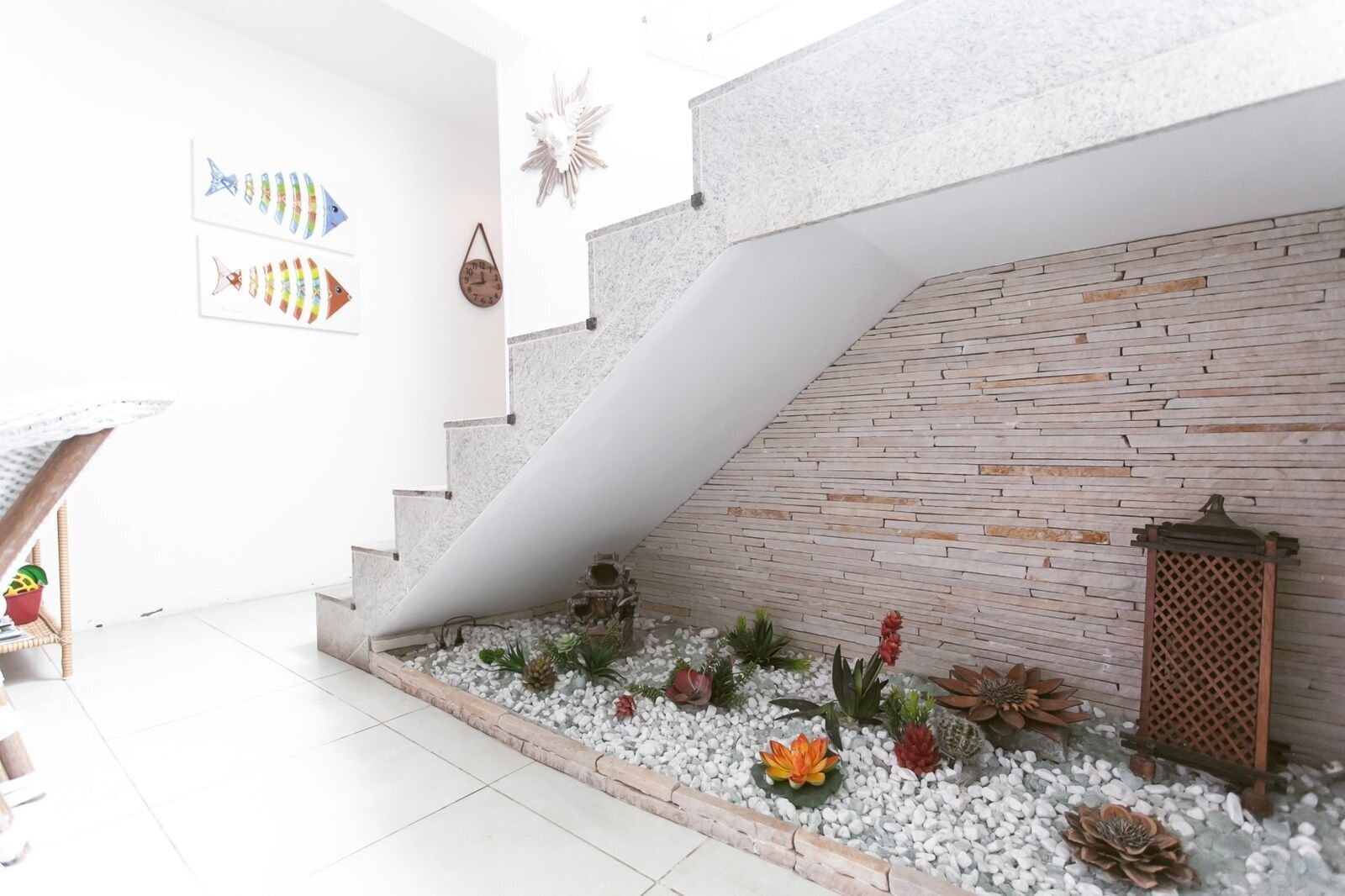 A modern interior with a staircase leading to a wooden wall, a small garden area with plants, and decorative items.