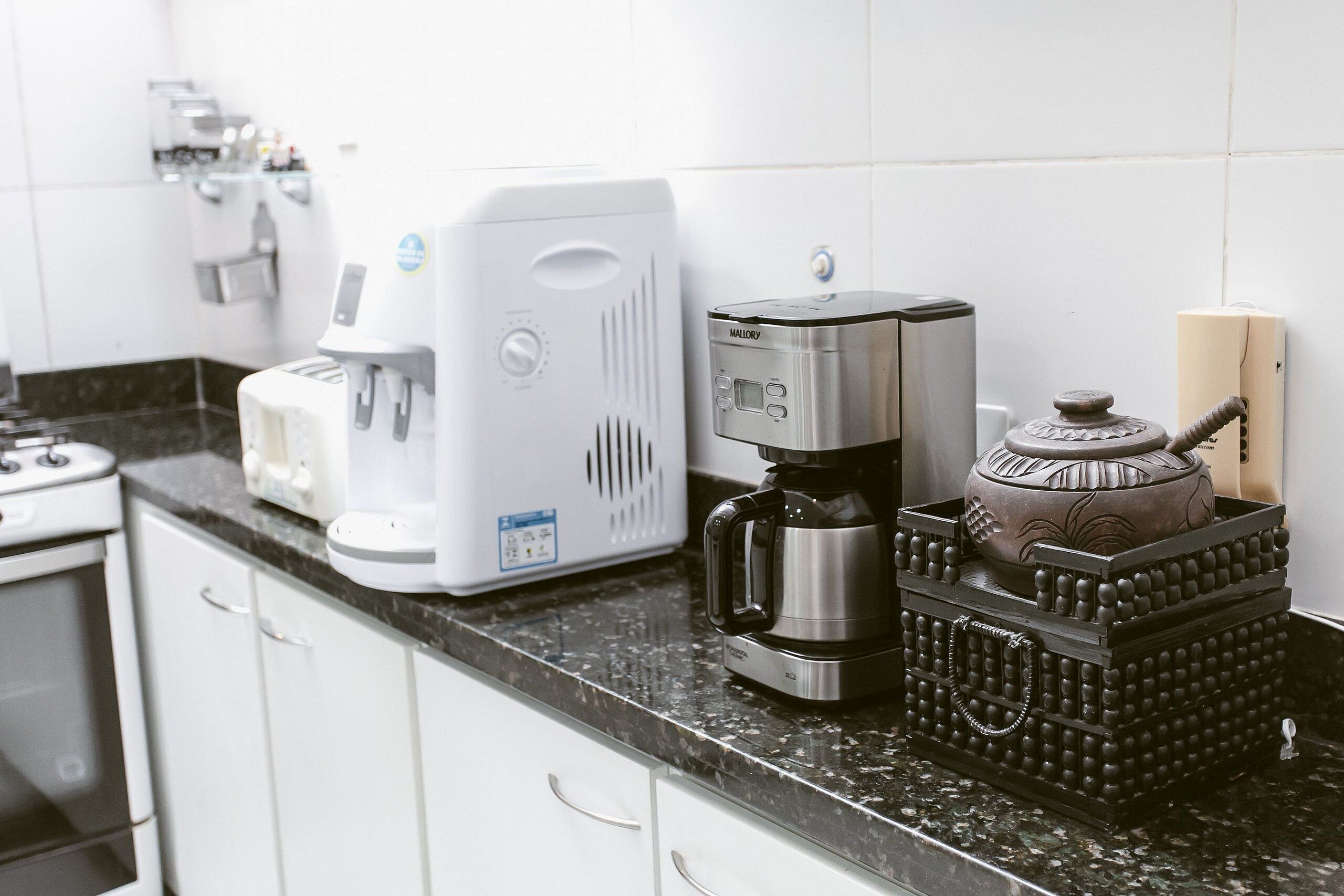 Ett kök med en kaffebryggare, en vattenkokare och en dekorativ behållare på bänkskivan.