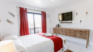 A hotel room with a bed, a TV, a dresser, and a balcony. - Bz24 Geribá 350 metros da praia 4 Suítes (Buzios)