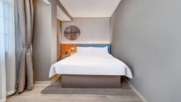 A modern hotel room with a large bed, a round wall decoration, and a nightstand. - Homeinn · neo (Haikou Qilou Old Street Donghu Road) (Haikou)