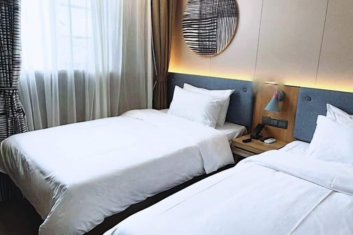 A hotel room with two beds, a bedside table with a lamp, and a wall-mounted light fixture.