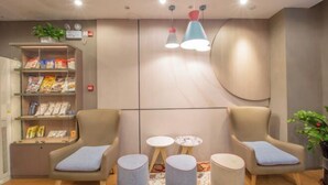 A modern lounge area with two armchairs, a small table, and a bookshelf with magazines and snacks. - Homeinn · neo (Haikou Qilou Old Street Donghu Road) (Haikou)