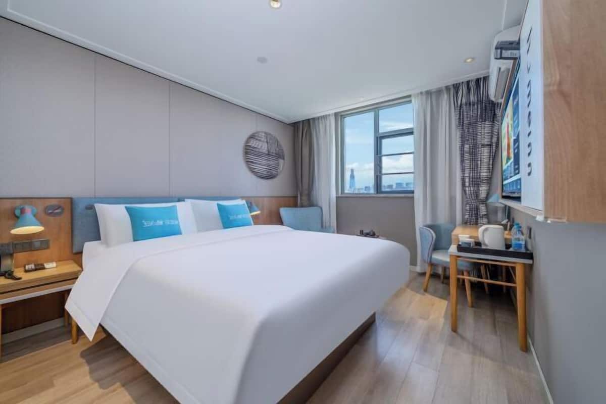 A modern hotel room with a large bed, a desk, and a view of the city skyline.
