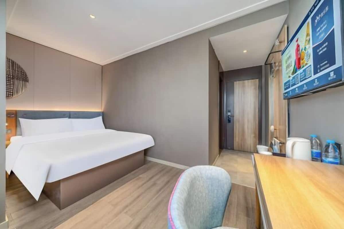 A hotel room with a bed, a desk, a chair, a TV, and a wall-mounted menu board.
