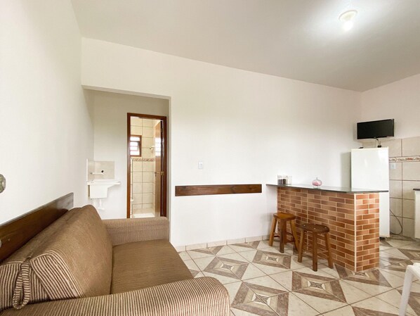 A living room with a sofa and a kitchen area with a brick counter and stools.