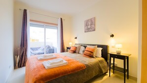 Une chambre d’hôtel avec un lit, deux lampes de chevet, une fenêtre avec des rideaux et une œuvre d’art accrochée au mur.