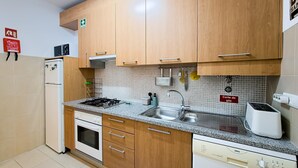 Une cuisine compacte dotée de meubles en bois, d’une cuisinière à gaz, d’un four encastré, d’un évier et d’un lave-vaisselle.