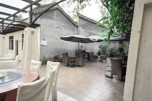 Een terras buiten met een ronde tafel en stoelen, omringd door potplanten en parasols.