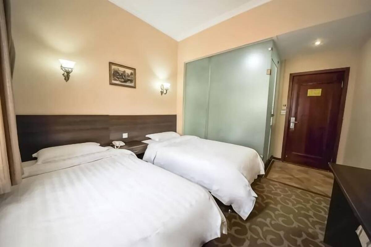 A hotel room with two beds, a wooden headboard, a nightstand, a telephone, a wall-mounted light fixture, and a door.