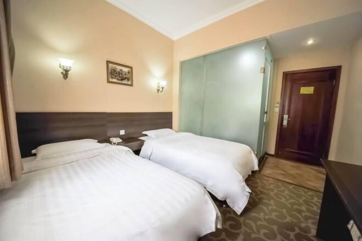 A hotel room with two beds, a nightstand, a wall-mounted light, and a door.