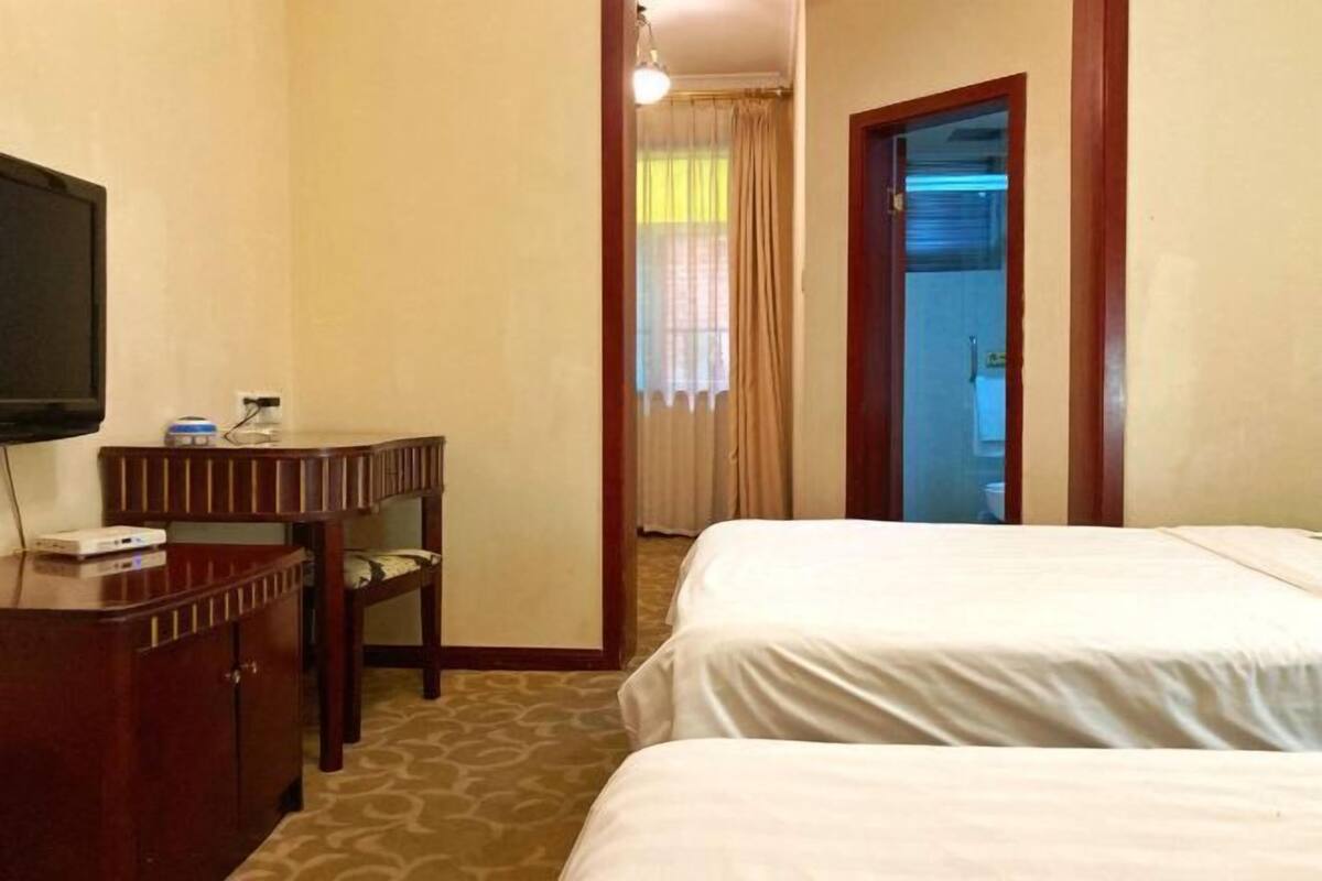 A hotel room with two beds, a desk with a television, and a door leading to a bathroom.