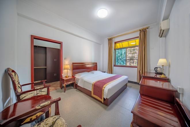 A hotel room with a bed, a desk, a chair, a wardrobe, and a window with curtains.