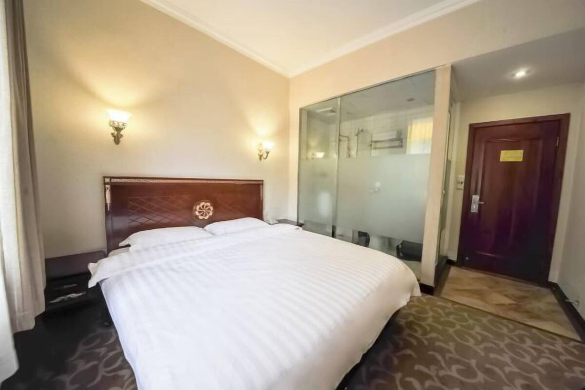 A hotel room with a bed, two wall sconces, a glass shower enclosure, and a door.