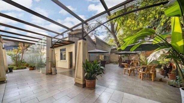 Un espace extérieur abrité, doté d’un sol carrelé, de plantes en pot et de mobilier en bois.