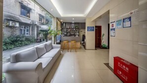 Un hall d’hôtel moderne avec un canapé, des tabourets de bar, un coin cuisine et une vue sur l’extérieur.