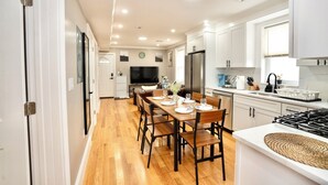 A modern kitchen with white cabinets, a dining table set for four, and a large flat-screen TV.