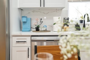 Una cocina con una cafetera, una orquídea en maceta y un bloque de cuchillos.