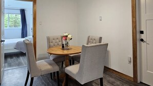 A dining area with a round table, four grey upholstered chairs, and a vase with flowers. - Escape to nature at Saltwater Hideaway Cottage. Panoramic views!! (Lawrencetown)