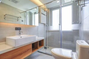 Moderni kylpyhuone, jossa on suuri peili, valkoinen pesuallas, lasinen suihkuseinä ja wc.