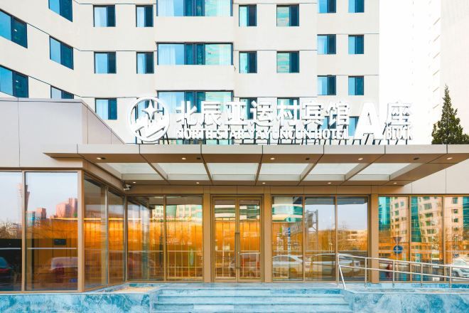 Ein moderner Hotelzugang mit Glasfassade, einer überdachten Vorfahrt und einer Treppe zum Eingang.