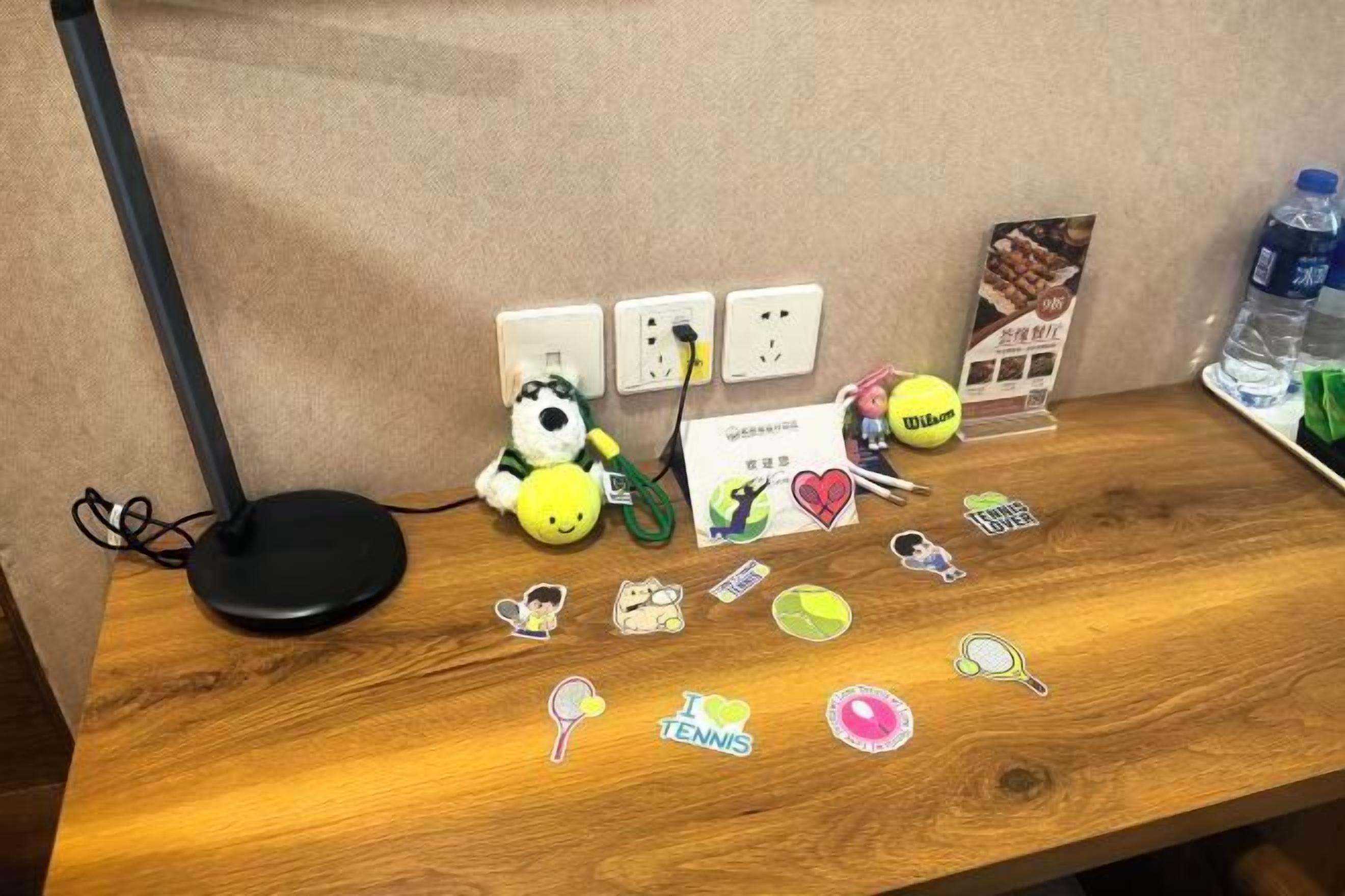 Uma mesa de madeira com uma lâmpada, um brinquedo de pelúcia, uma bola de tênis e diversos adesivos.