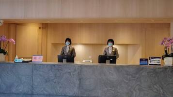 A reception desk with two staff members, a marble counter, and a potted plant.
