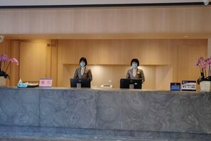 A reception desk with two staff members, a marble counter, and a potted plant. - Yayuncun Hotel (Beijing)